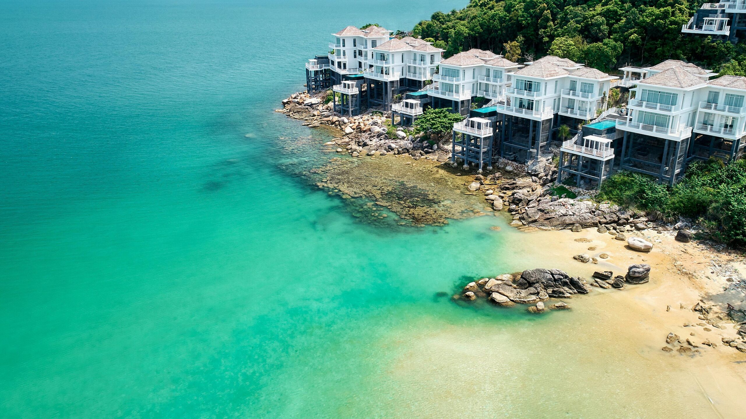 Luxury villas perched on a rocky coast with turquoise sea, offering a tropical paradise feel.
